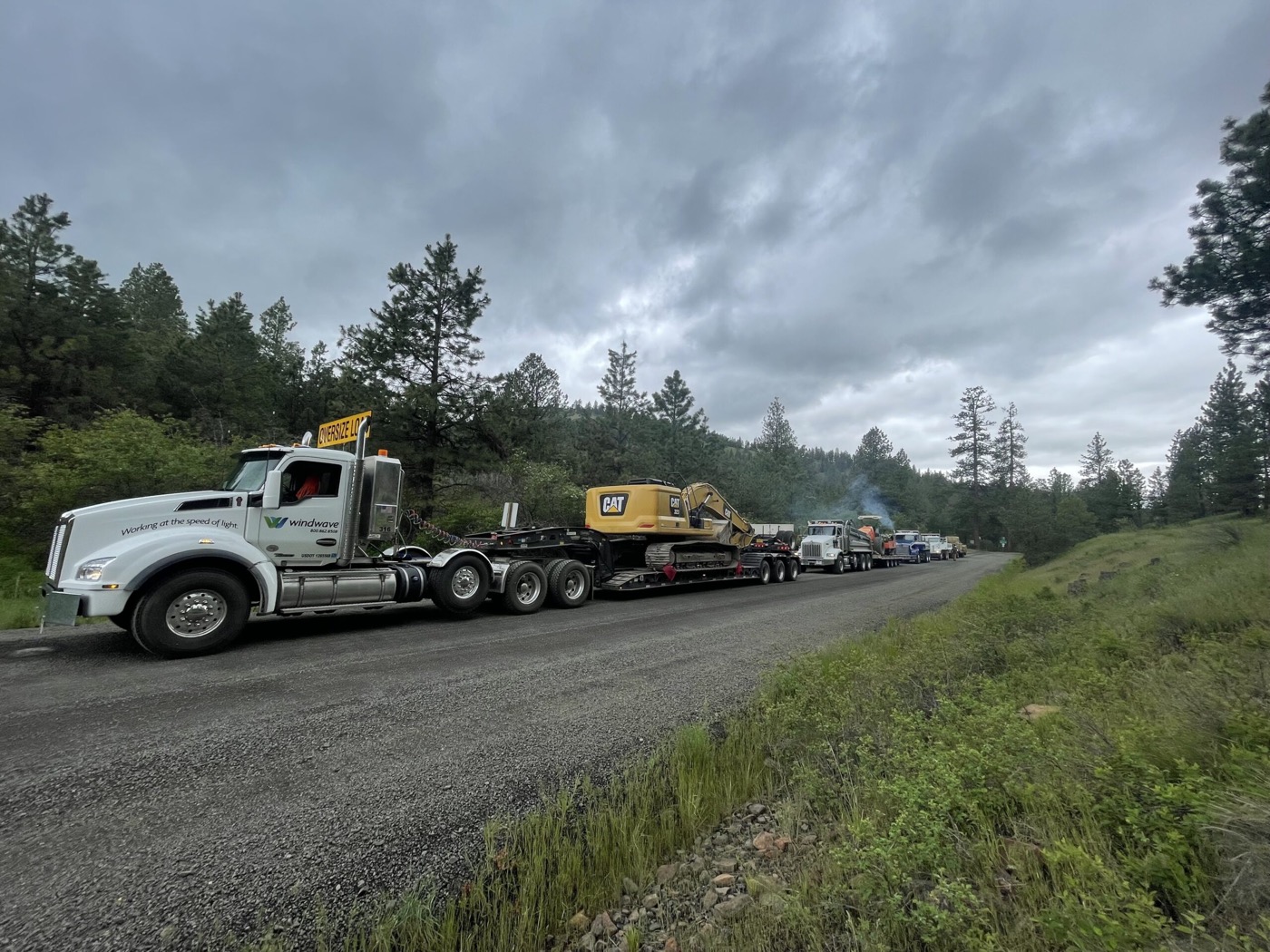 Excavator on a lowboy trailer heading out to a job along a forest highway