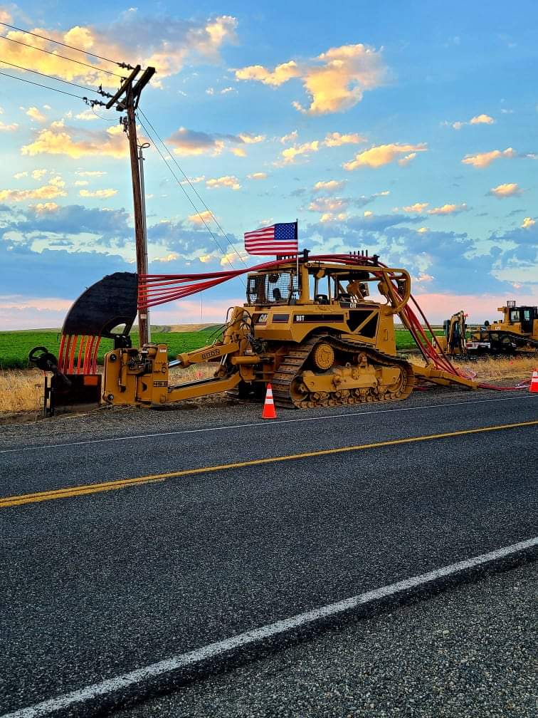 Cable plough placing conduit at sunrise, the American flag flying from the tractor